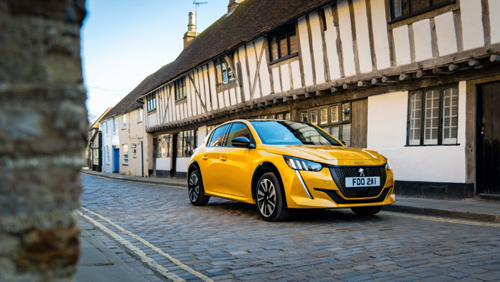 A bright yellow 2024 Peugeot 208 parked on a quiet street in Faversham with historic Kentish buildings in the background, representing cheap car rental.