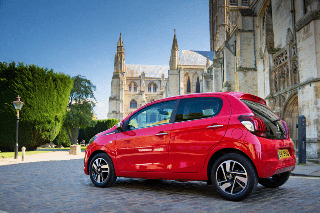 Red hire car parked in front of Canterbury Cathedral, showcasing the vehicle's design and the historic architecture of the city.